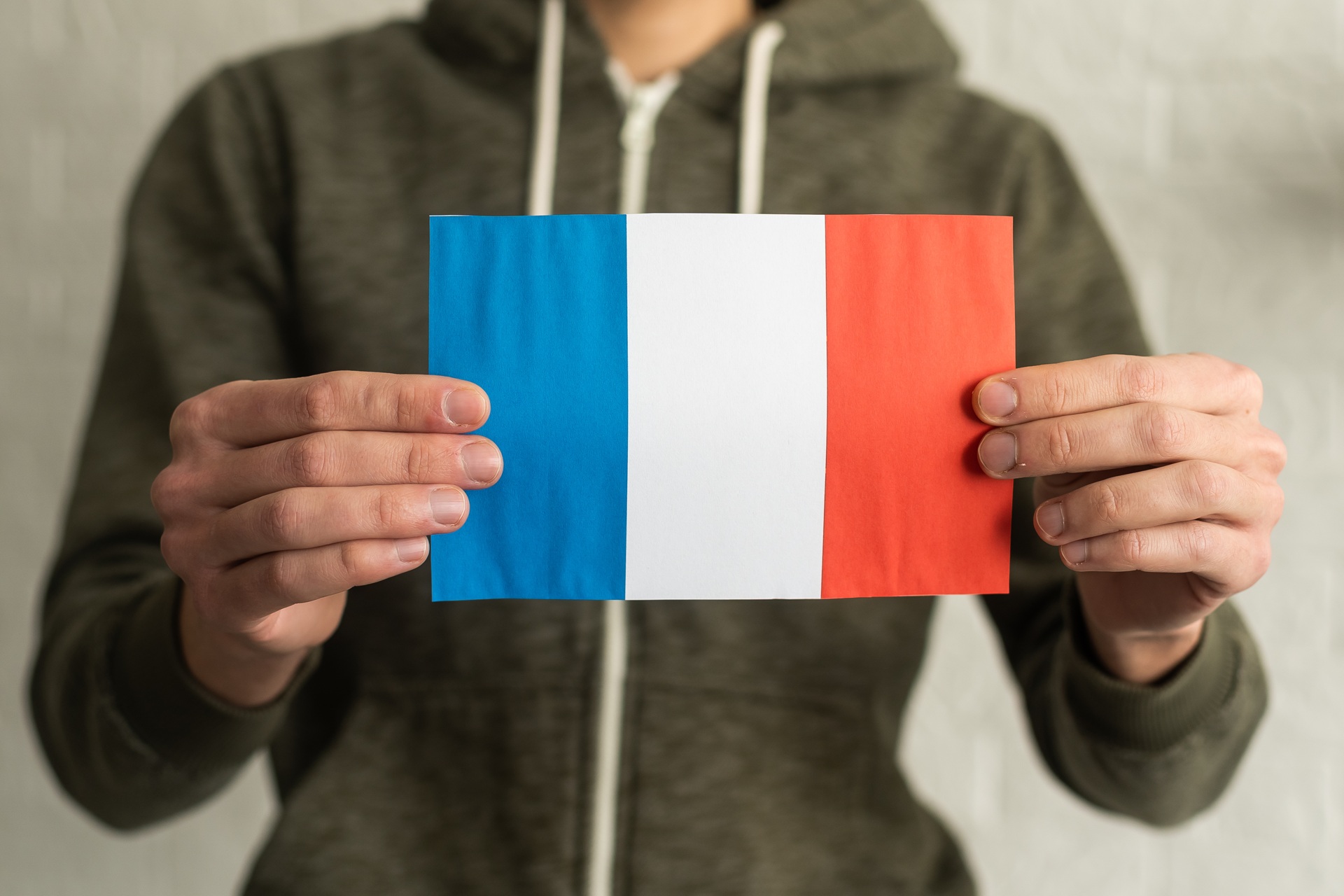 A person in a green hooded sweatshirt holding a French flag with two hands.